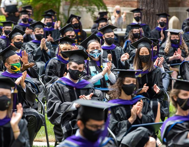 Graduates wear caps and gowns at an outdoor ceremony
