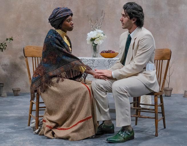 Two actors seated at a table on stage