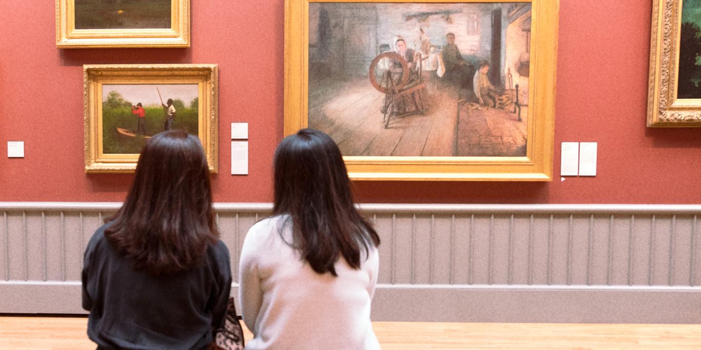 two people sitting on a bench looking at paintings on the wall