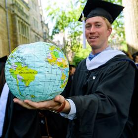 A Yale student wearing a cap and gown holds out a globe