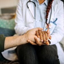 A caretaker holds the hand of a patient