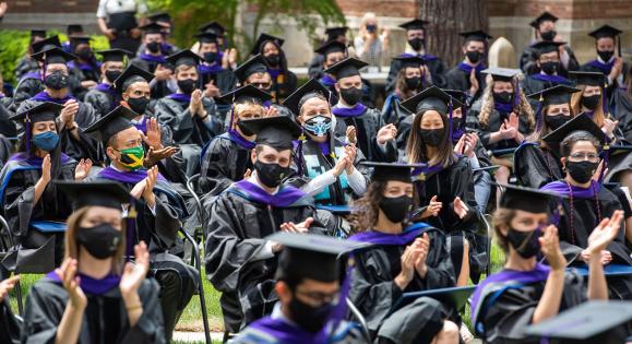 Graduates wear caps and gowns at an outdoor ceremony