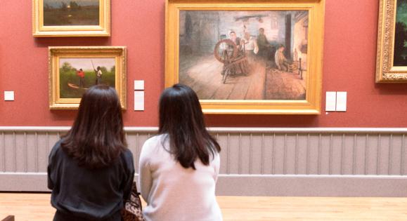 two people sitting on a bench looking at paintings on the wall