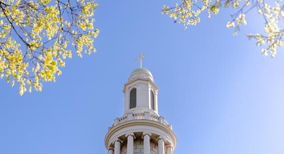 Top of Divinity School building with blue sky in background and tree branches in foreground 
