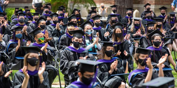 Graduates wear caps and gowns at an outdoor ceremony