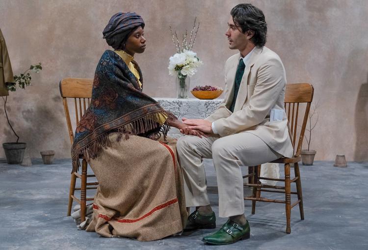 Two actors seated at a table on stage