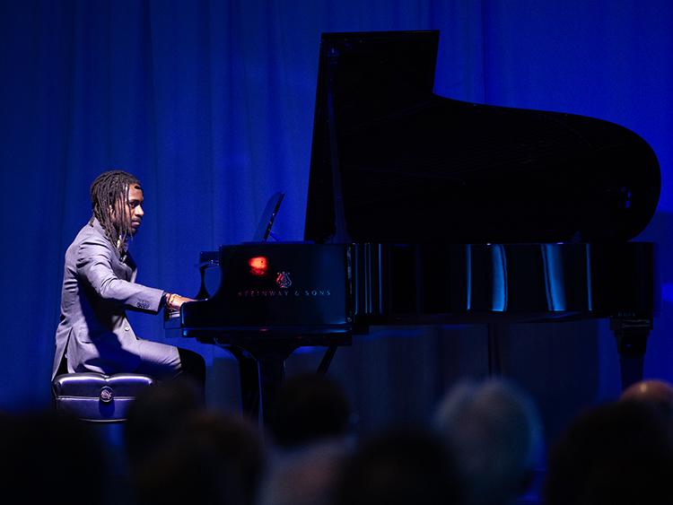AZA Allsop performing a musical meditation on stage with a piano at the For Humanity Illuminated Chicago event