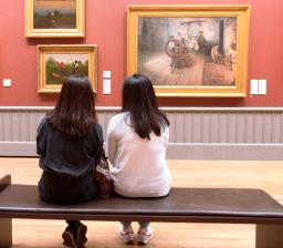 two people sitting on a bench looking at paintings on the wall
